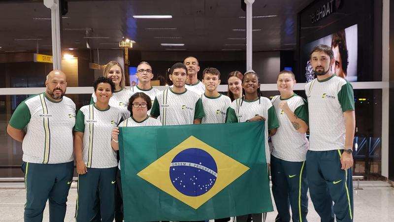 female Para taekwondo fighter Debora Menezes with other fighters holding a Brazilian flag