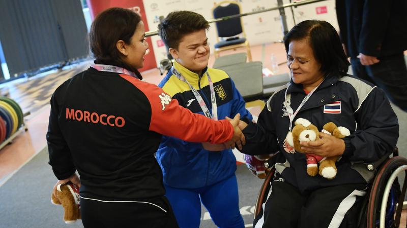 three female powerlifters shaking hands together on the podium