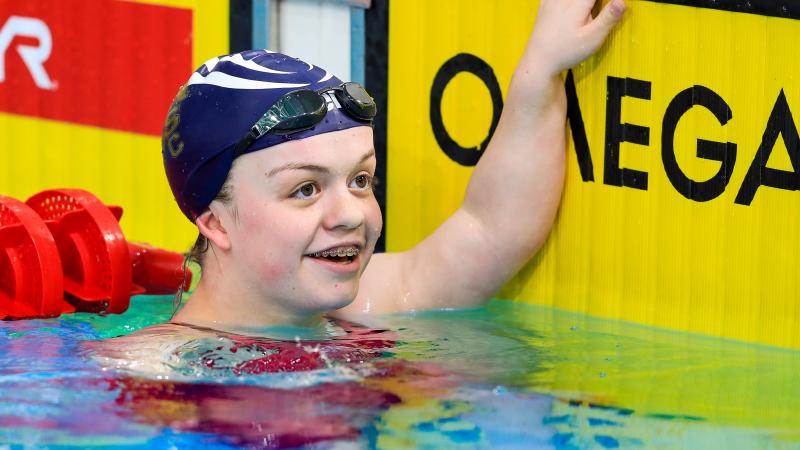 female Para swimmer Maisie Summers-Newton holds onto the wall and smiles in the pool at the end of the race