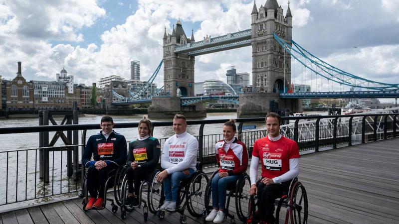 Five wheelchair athletes sitting in a row at the edge of the River Thames with London's Tower Bridge in the background