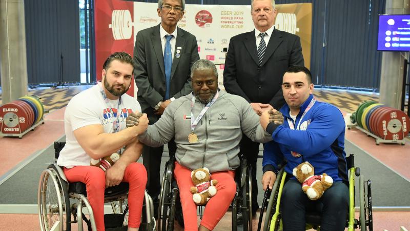 male Para powerlifter Mohammed Khamis Khalaf in the middle of two other powerlifters on the podium with their arms around eachother 