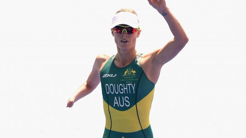 female Para triathlete Kate Doughty raises her hand and points to the sky as she crosses the finish line
