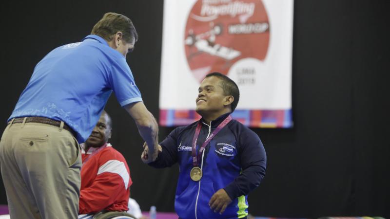 male Para powerlifter Herbert Aceituno shaking hands with an official