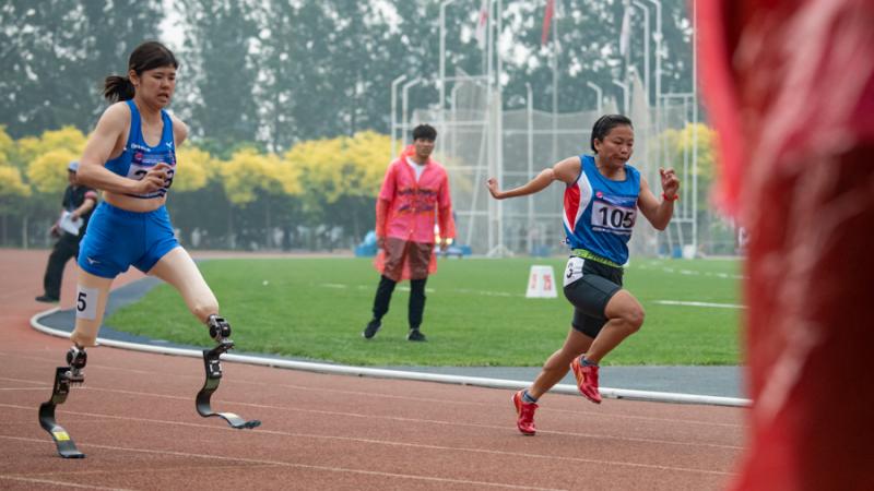 A double-leg amputee woman running against another woman on an athletics track