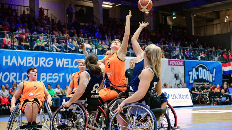 female wheelchair basketball players from Netherlands and Great Britain reaching up for the ball