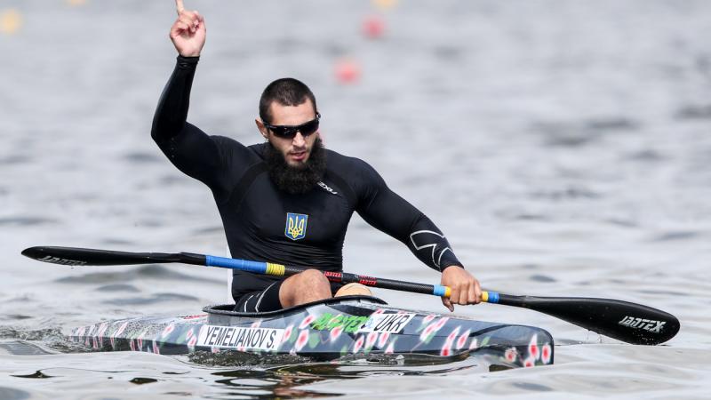 Serhii Yemelianov celebrates in the canoe with his hand in the air after winning gold