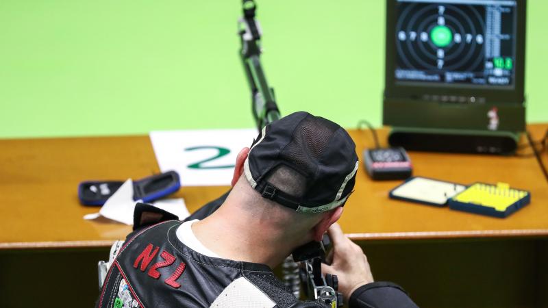 A man seated seen from behind while shooting with a rifle