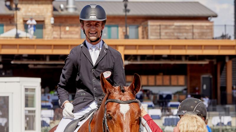 Latvian male dressage rider with celebral palsy smiles on a horse