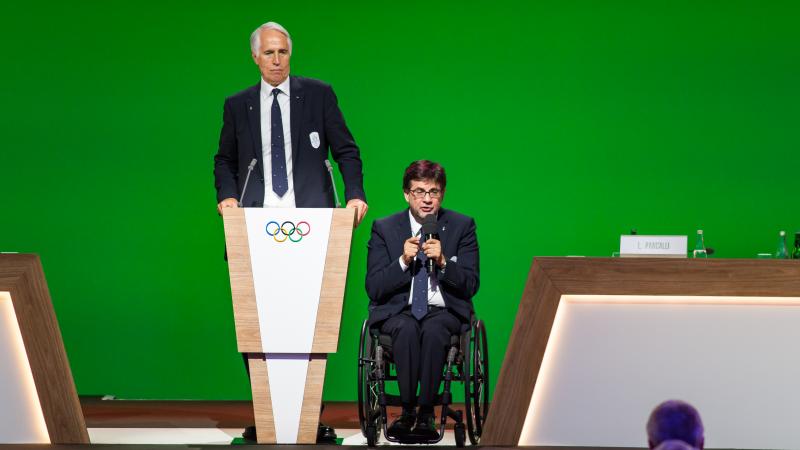 A man standing and another man in a wheelchair on stage