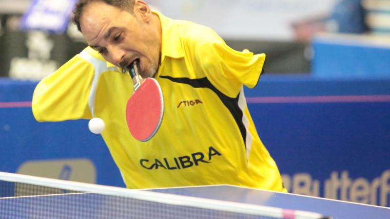 Egyptian male table tennis player holds racket in mouth and attempts to hit the ball