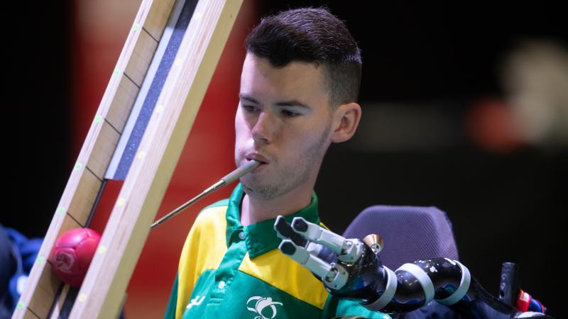Australian male boccia player holds device in mouth to push ball down ramp
