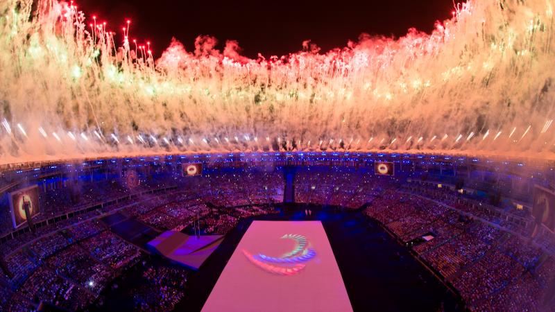 a high shot of the Olympic Stadium in Rio with fireworks going off and the Agitos symbol on the floor
