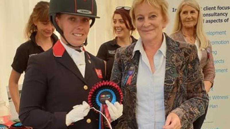 British female dressage athlete holds bucket of prize with an organiser