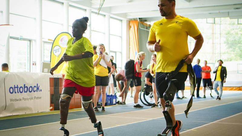 Male sprinter with prothesis runs alongside a young double-amputee sprinter girl