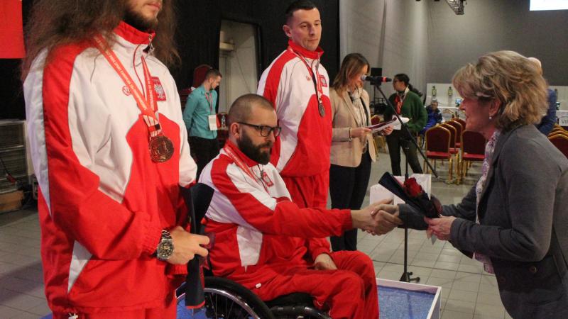 Man in wheelchair shakes hand with woman during medal ceremony