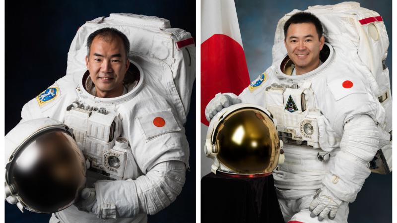 two male astronauts smiling in their space suits and standing beside the Japan flag