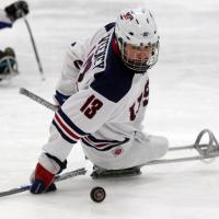 A picture of a man in a sledge playing ice hockey
