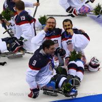 Four sledge hockey player on the ice, posing for a camera with their gold medals