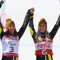 a female vision impaired skier and her guide raise their arms in celebration