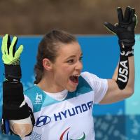 a female sit skier throws up her arms in celebration