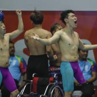 three male Para swimmers celebrate at the edge of the pool 