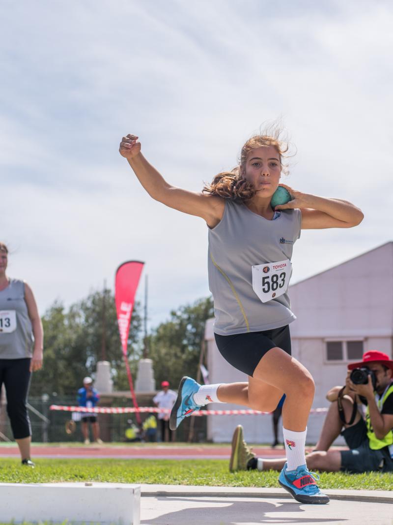 A female teenage athlete competing in shot put watched by three people