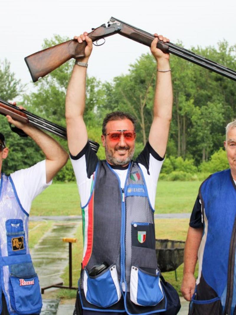 Three male Para trap shooters pose together with man in middle raising his shot gun over his head