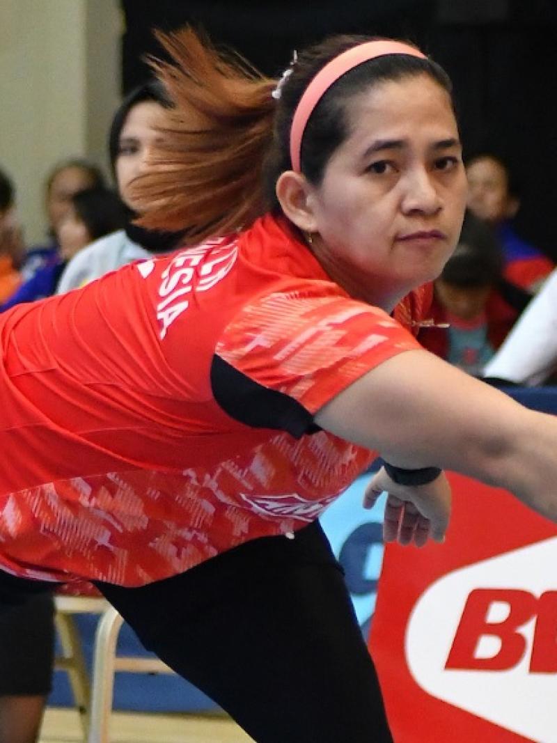A female Para badminton player leans down to hit a forehand
