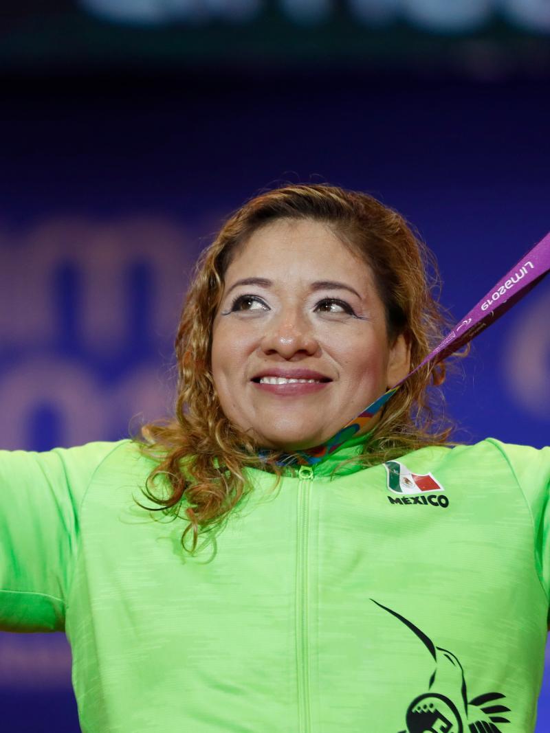 a female powerlifter holds up her gold medal and points her fingers to the sky