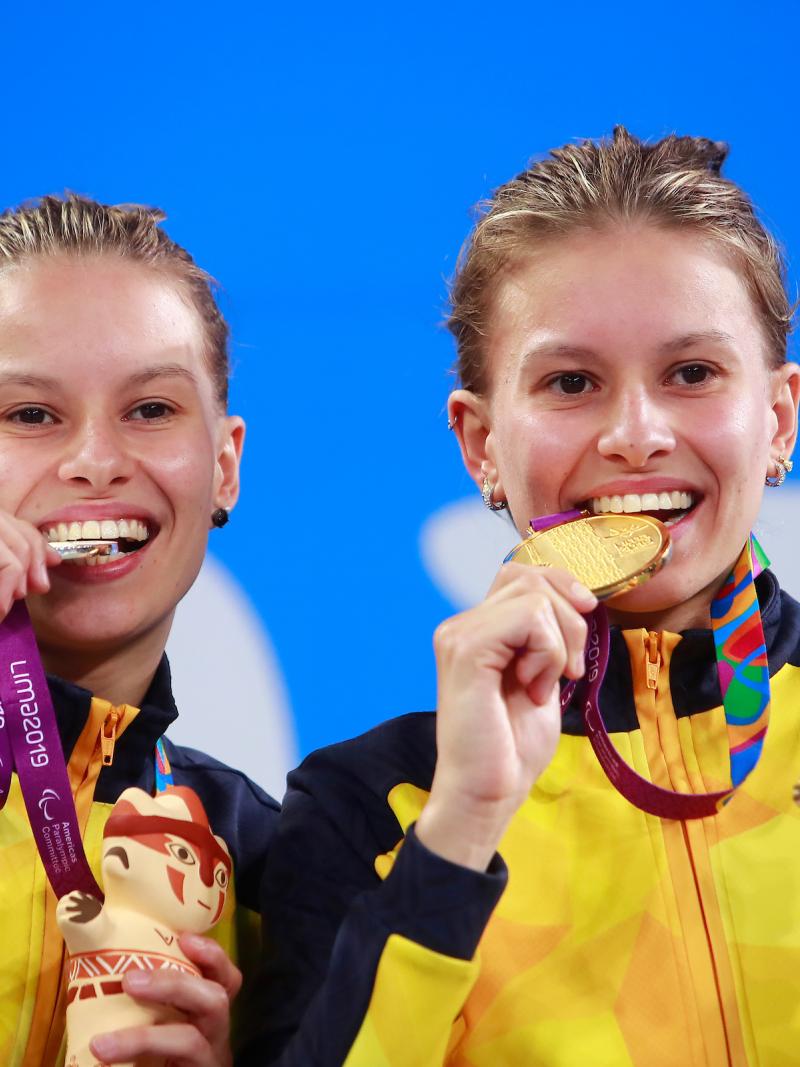 two female Para swimmers on the podium biting their medals