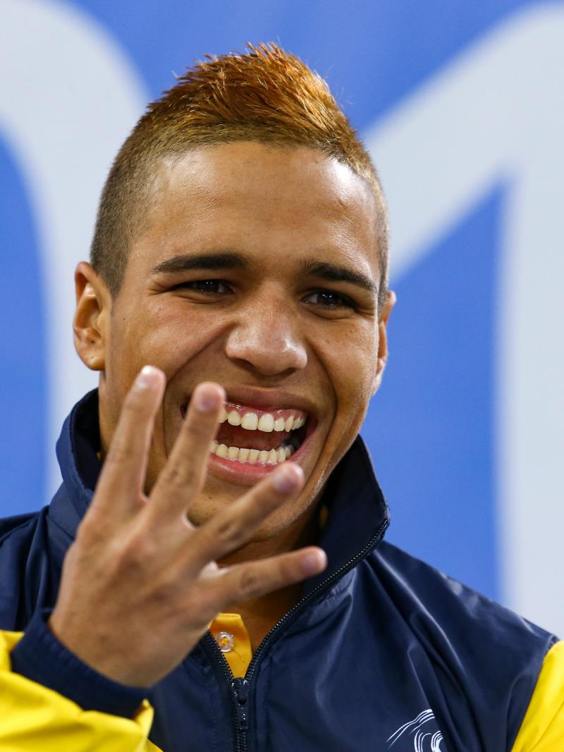 a male Para swimmer holds up four fingers and his gold medal