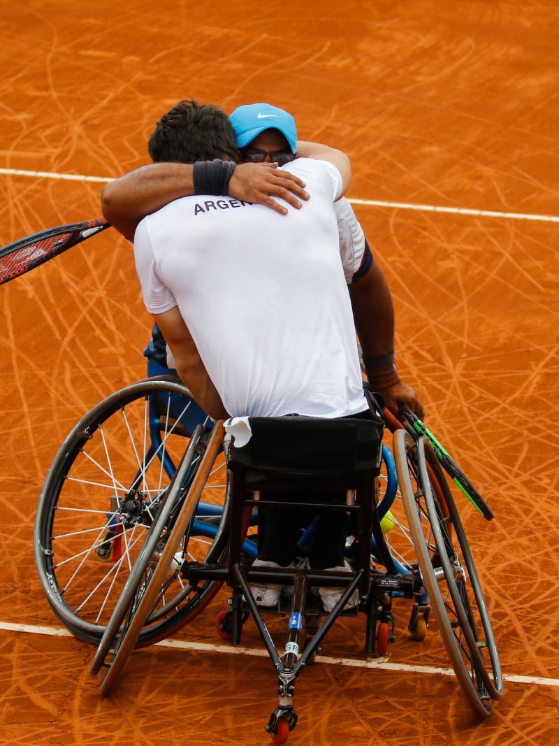 two male wheelchair tennis players hug on the court