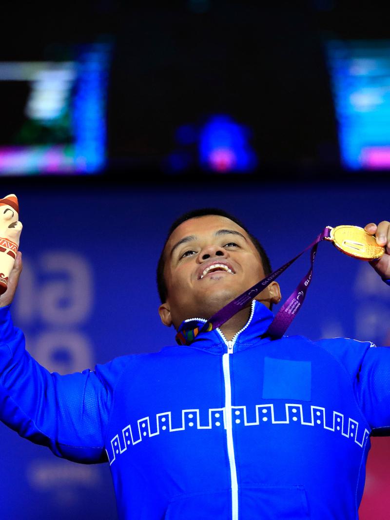 a male powerlifter holds up his gold medal