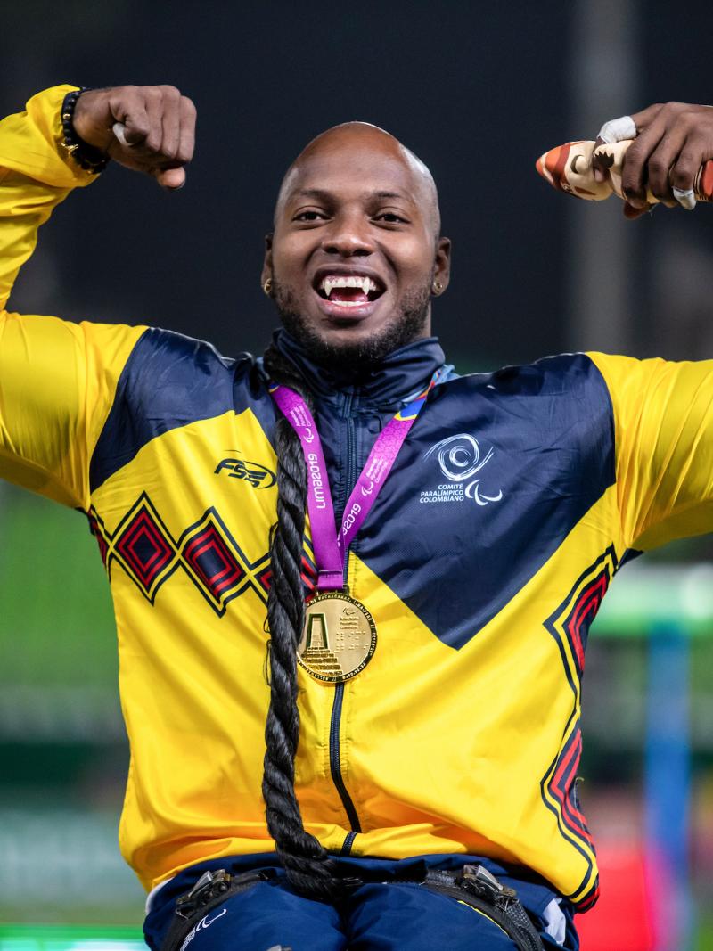 a male wheelchair athlete with a gold medal round his neck raises his arms