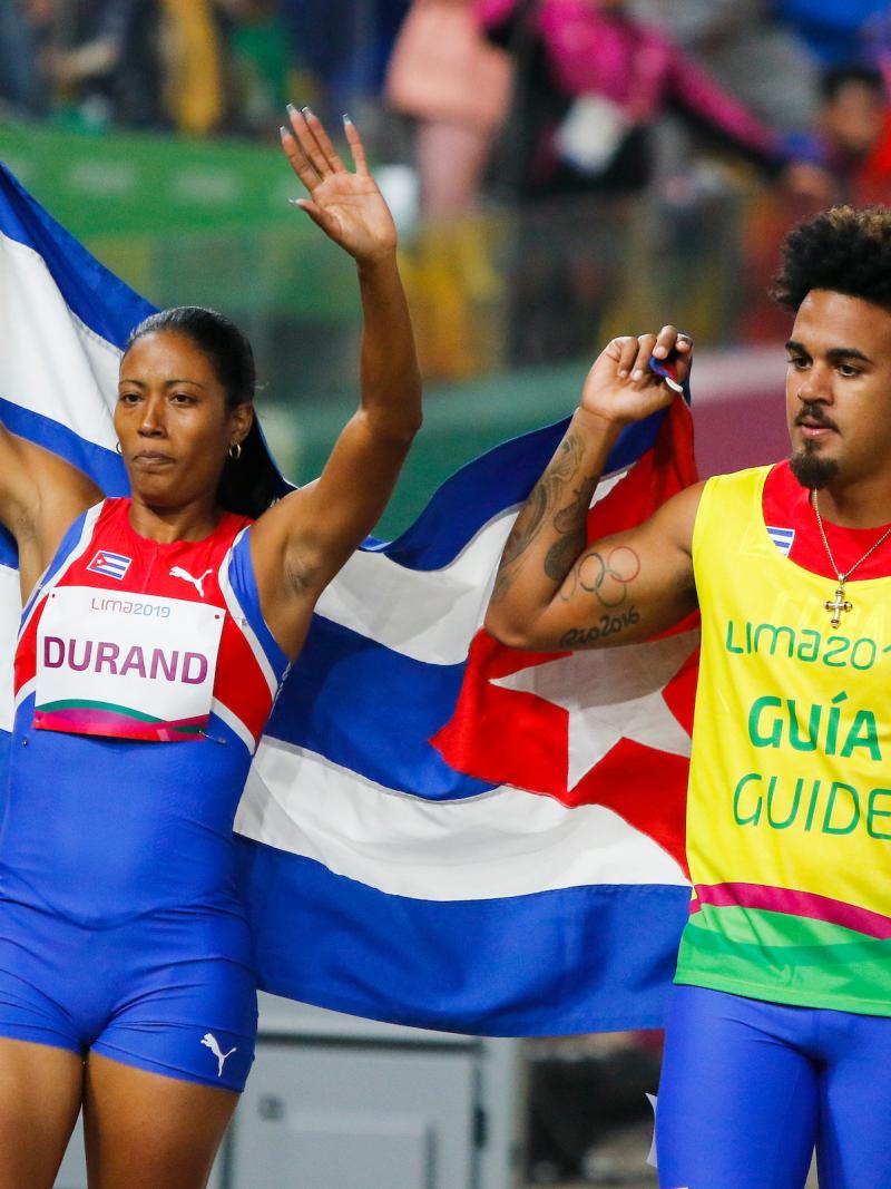 a female vision impaired runner and her male guide hold up the Cuba flag and wave