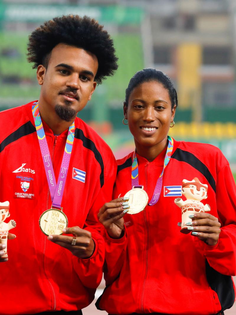 a female vision impaired runner and her guide hold up their gold medals