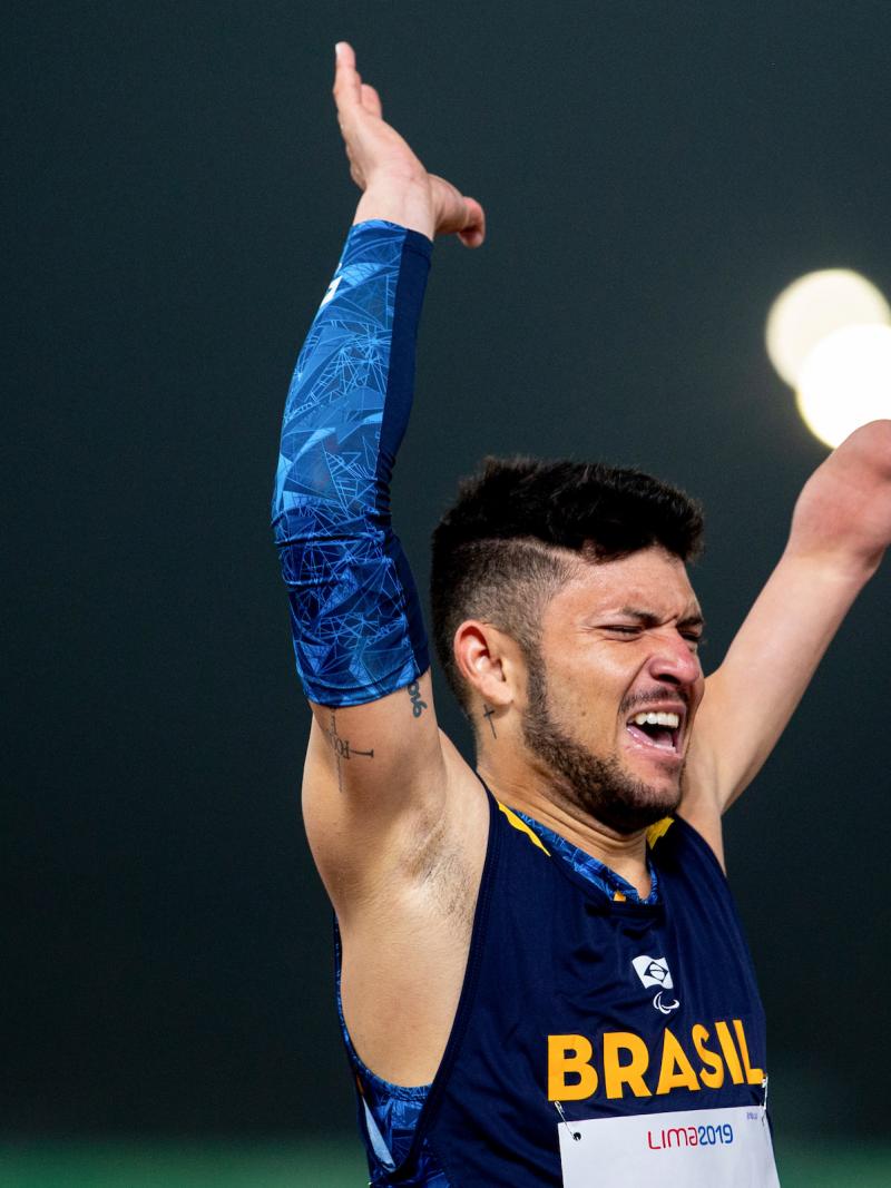 a male Para athlete throws his arms up in the air in celebration