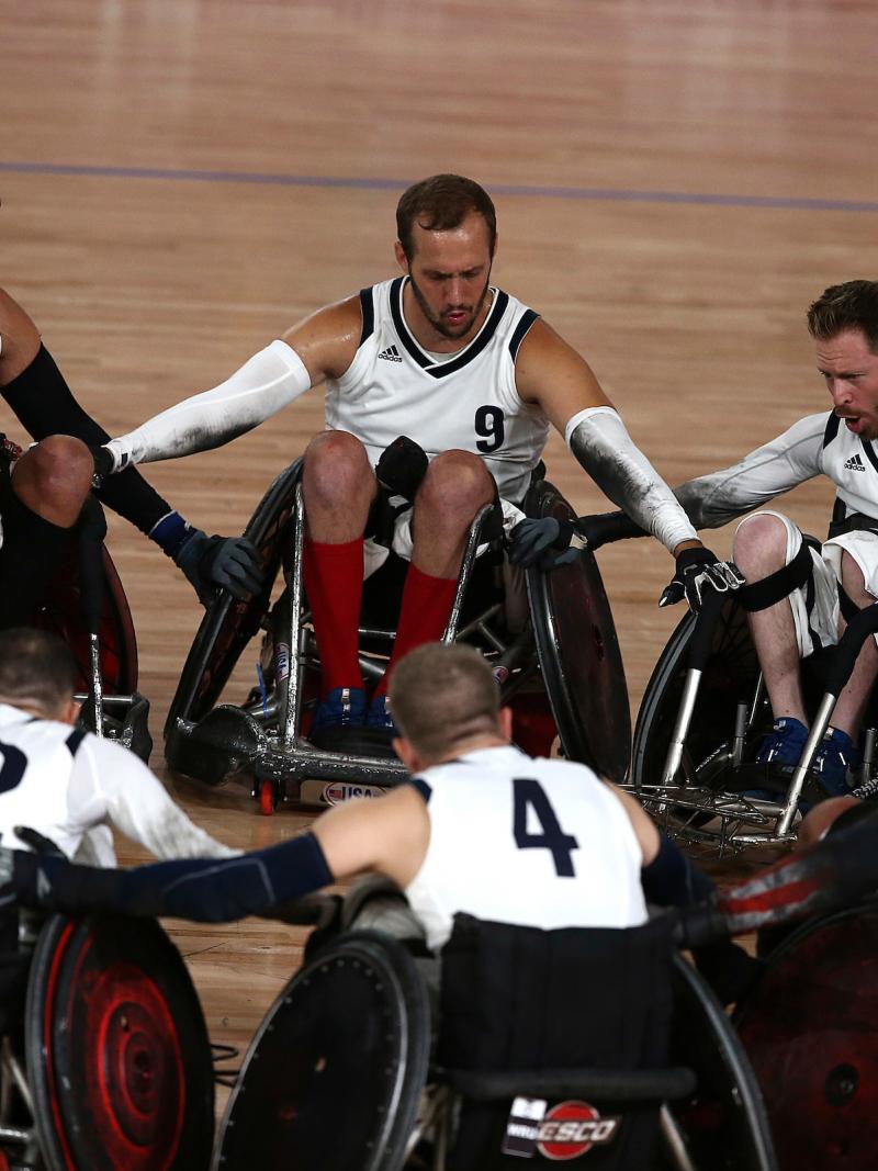 a group of male wheelchair rugby players in a circle holding arms