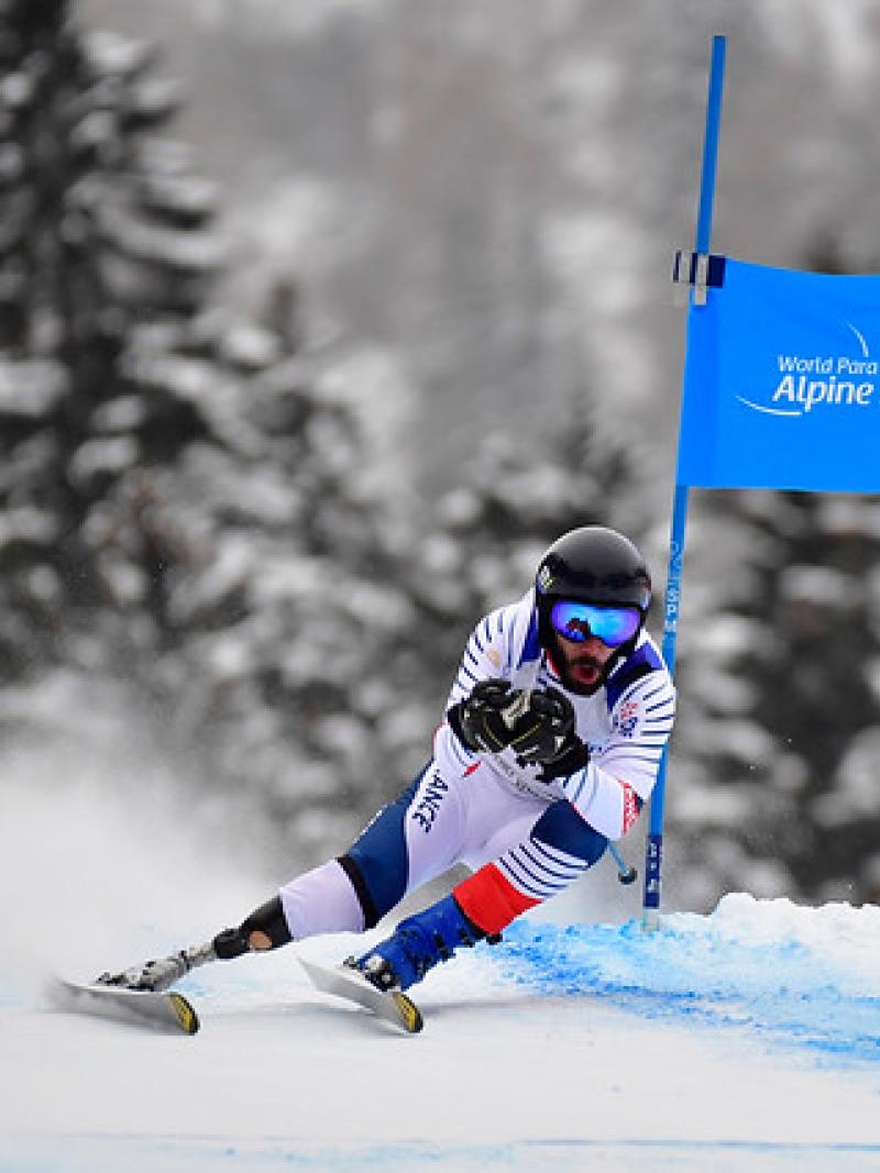 a male Para alpine skier with a prosthetic skiing round a gate