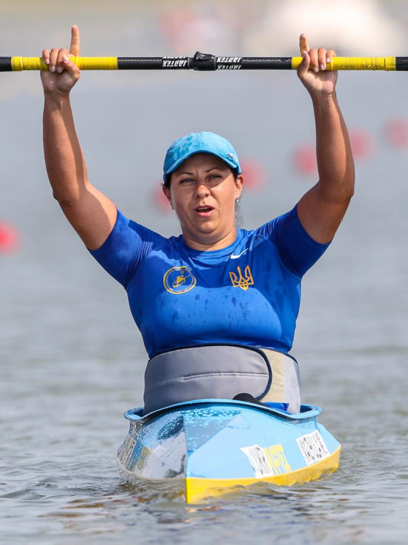 Woman in kayak raises paddle over her head