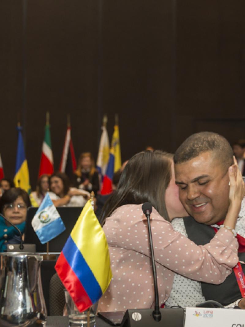 a man sitting at a desk smiling and being hugged by a woman