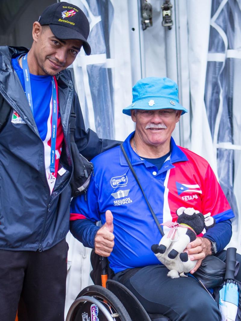 two men, one standing, one sitting in a wheelchair giving a thumbs up