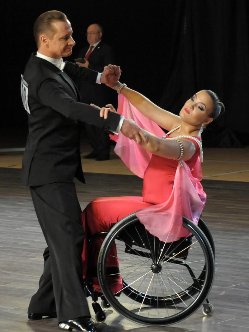 Male standing dancer performs standard dance with female partner in wheelchair