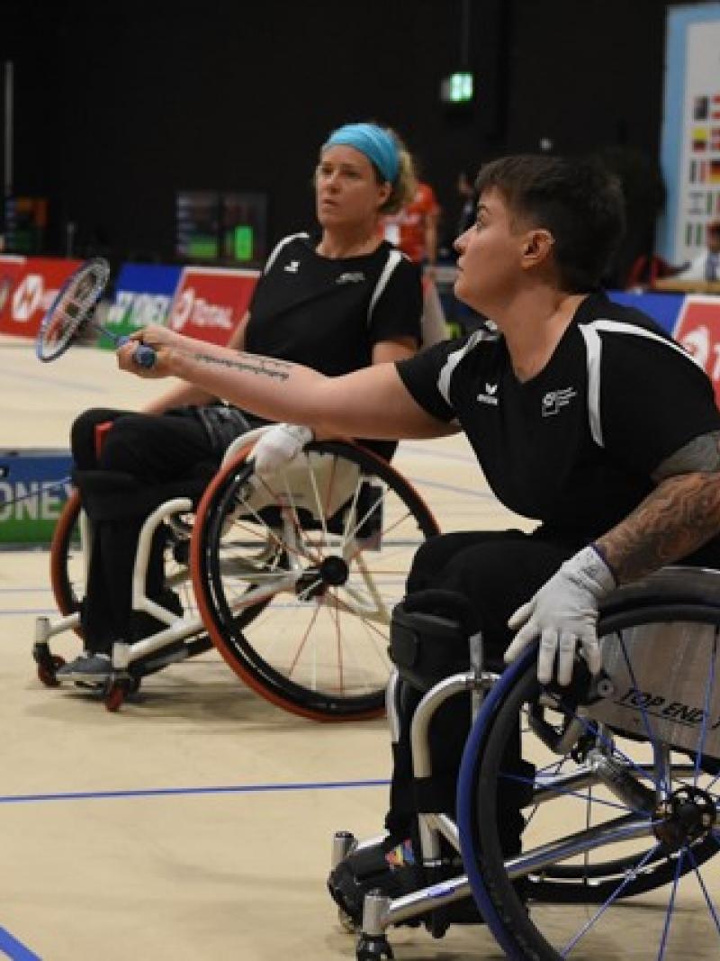 Two females in wheelchairs play badminton 