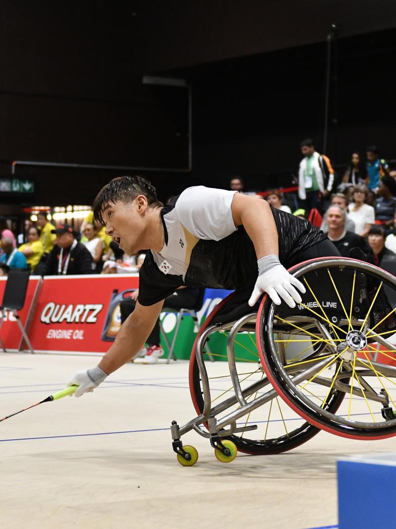South Korean man in wheelchair leans over to hit the badminton birdie