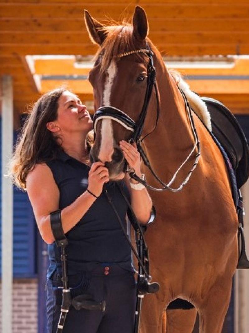 A female Para equestrian rider on crutches holds the bridle of her horse