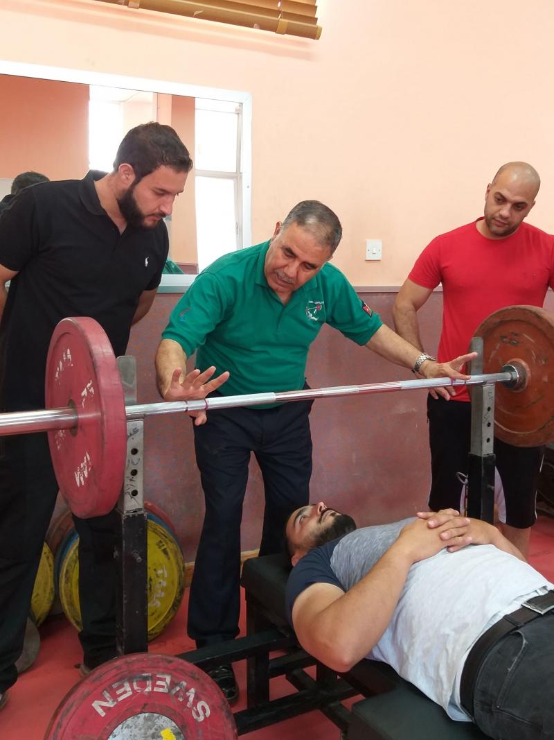 a group of officials standing round an athlete lying on a powerlifting bench
