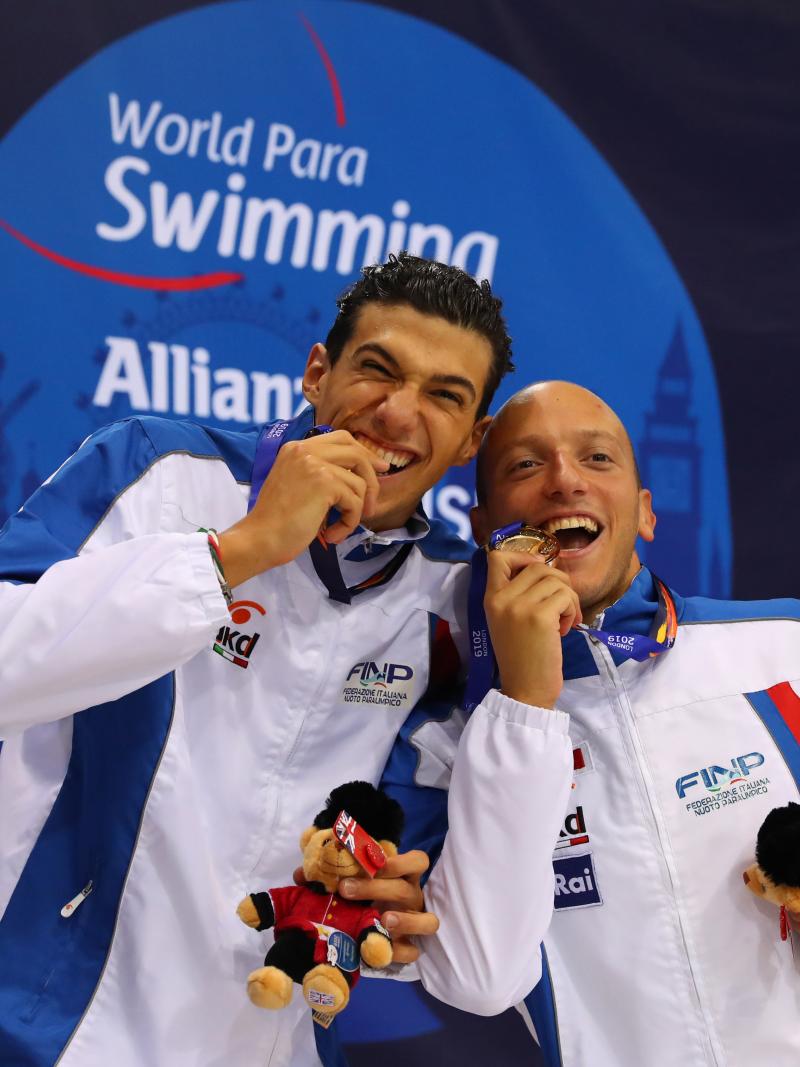 two male Para swimmers biting their medals