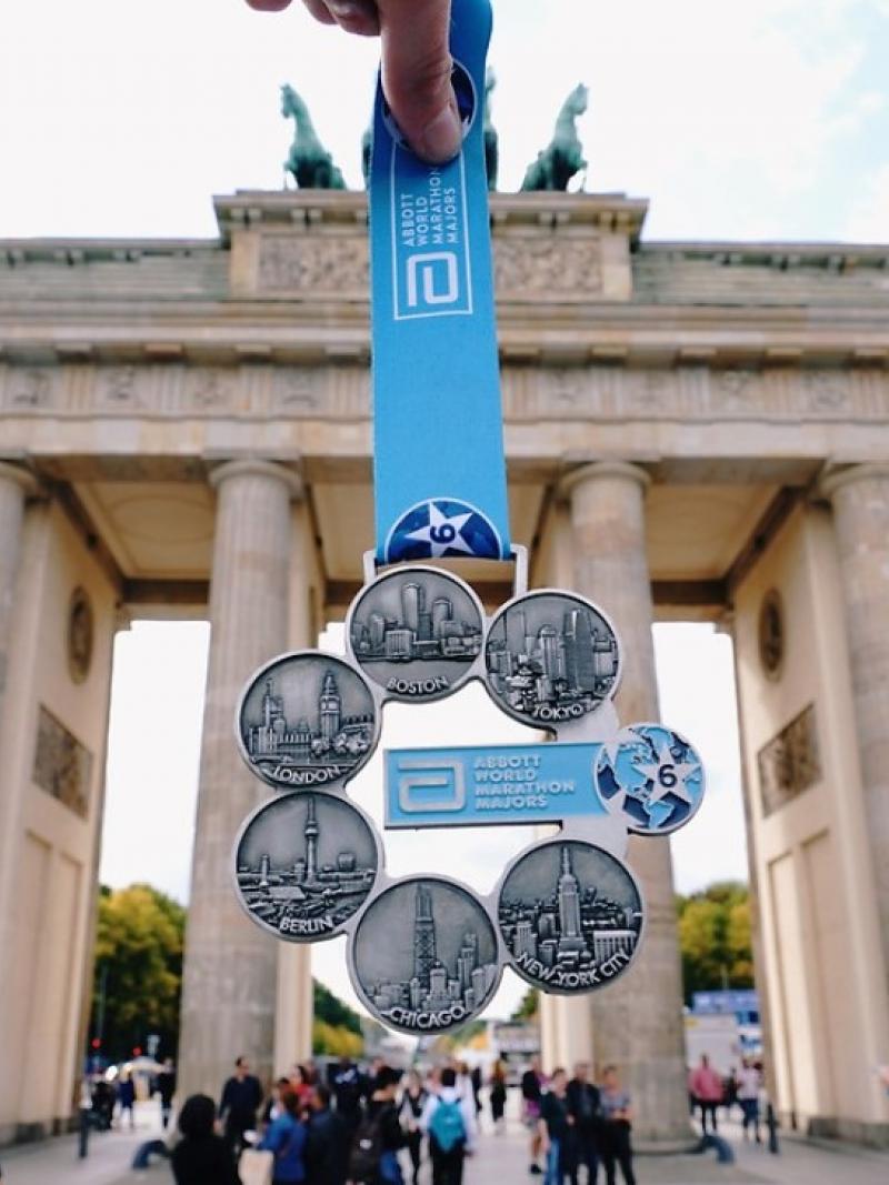 A marathon medal being shown in front of the Brandenburg Gate in Berlin