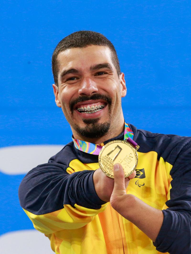 a male Para swimmer holds up his gold medal